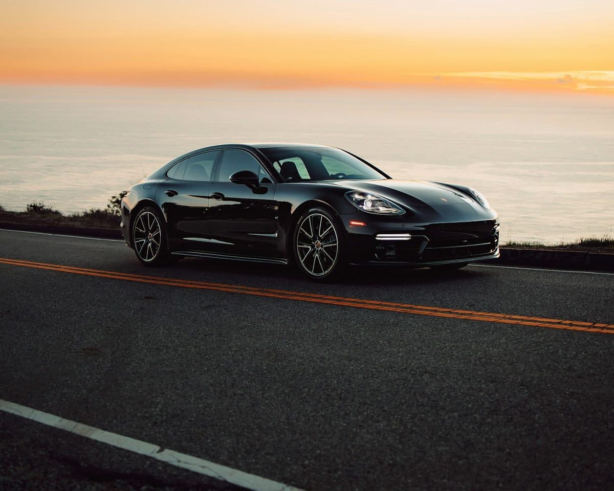 A black sports sedan on a coastal road at sunset
